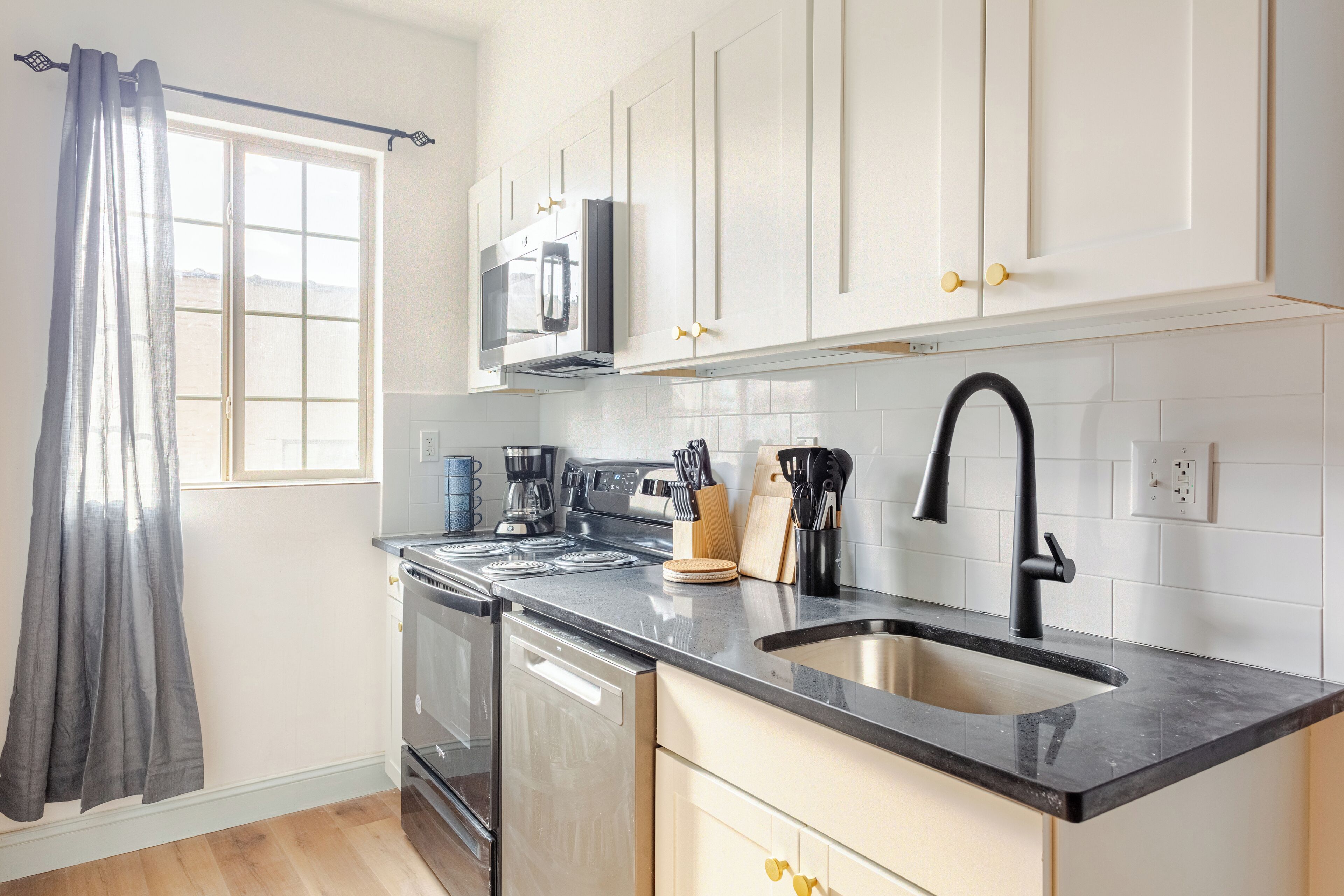 A modern kitchen with white cabinets, a black sink, and stainless steel appliances.