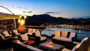 Una terraza con mobiliario exterior y vistas a un cuerpo de agua y montañas.