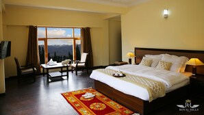 A hotel room with a large bed, a desk, a chair, and a view of mountains. - Royal Hills Ladakh (Leh)