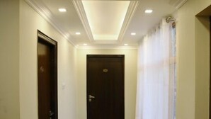 A hallway with a polished floor, a dark door at the end, and a window with white curtains. - Royal Hills Ladakh (Leh)