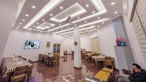 A hotel lobby with a modern ceiling design, multiple dining tables, and a seating area. - Royal Hills Ladakh (Leh)