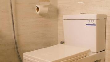 Un baño moderno con inodoro, ducha y un dispensador de papel higiénico en la pared.