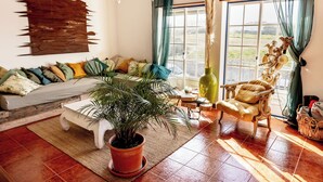 Una sala de estar acogedora con un sofá, una butaca, una planta en maceta y un amplio ventanal con cortinas.