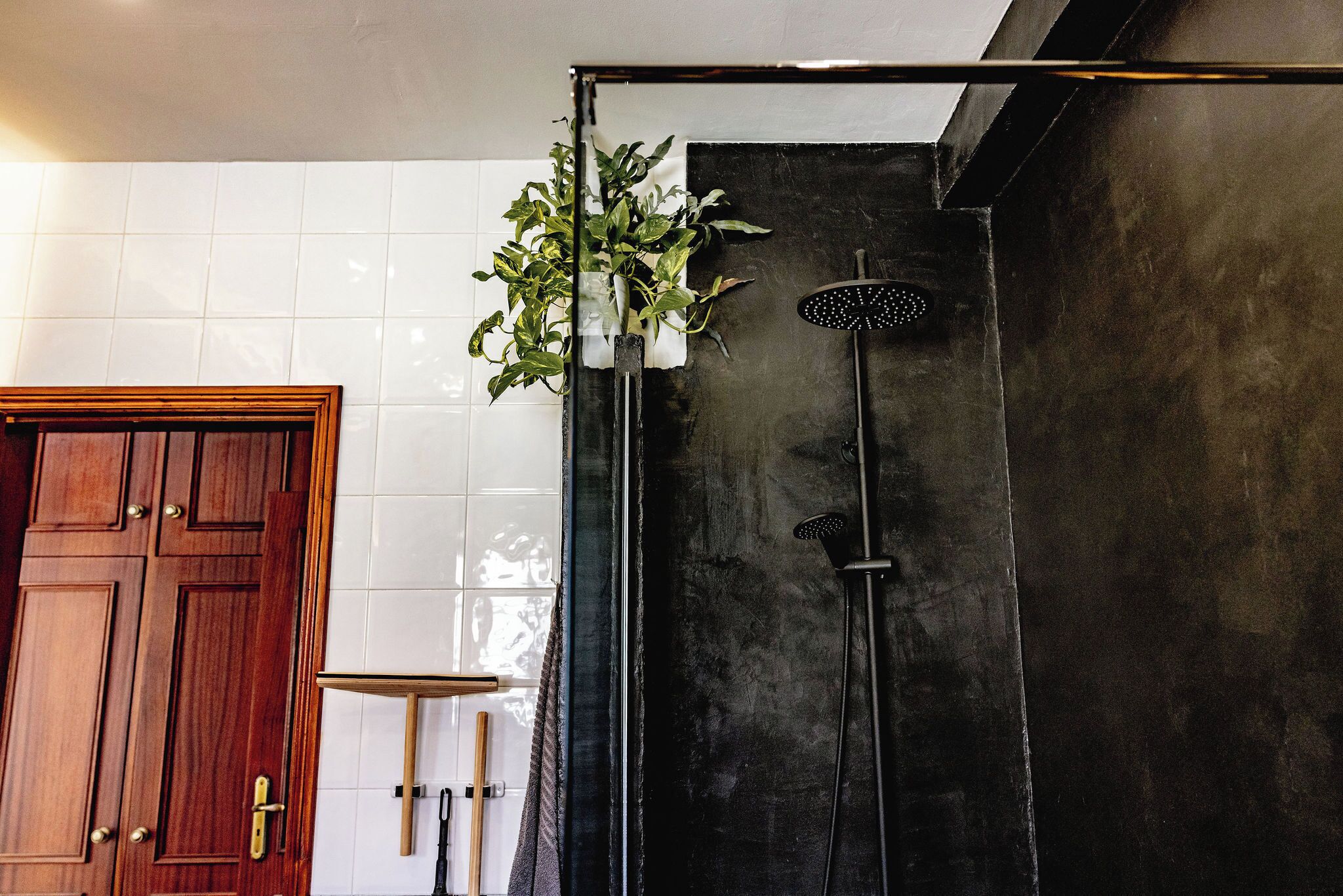 Un baño con puerta de madera, ducha con pared negra y una planta en maceta.