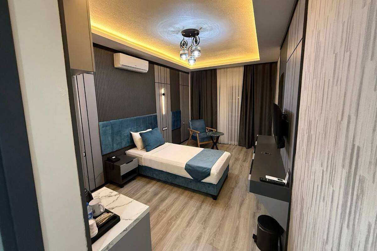 Una camera d'albergo moderna con un letto, una scrivania, una sedia, una televisione e una lampada a soffitto.