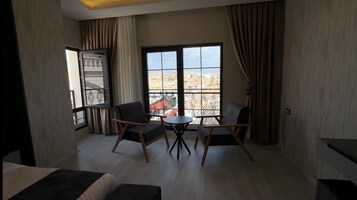 A room with a balcony, two chairs, a small table, and a bed.