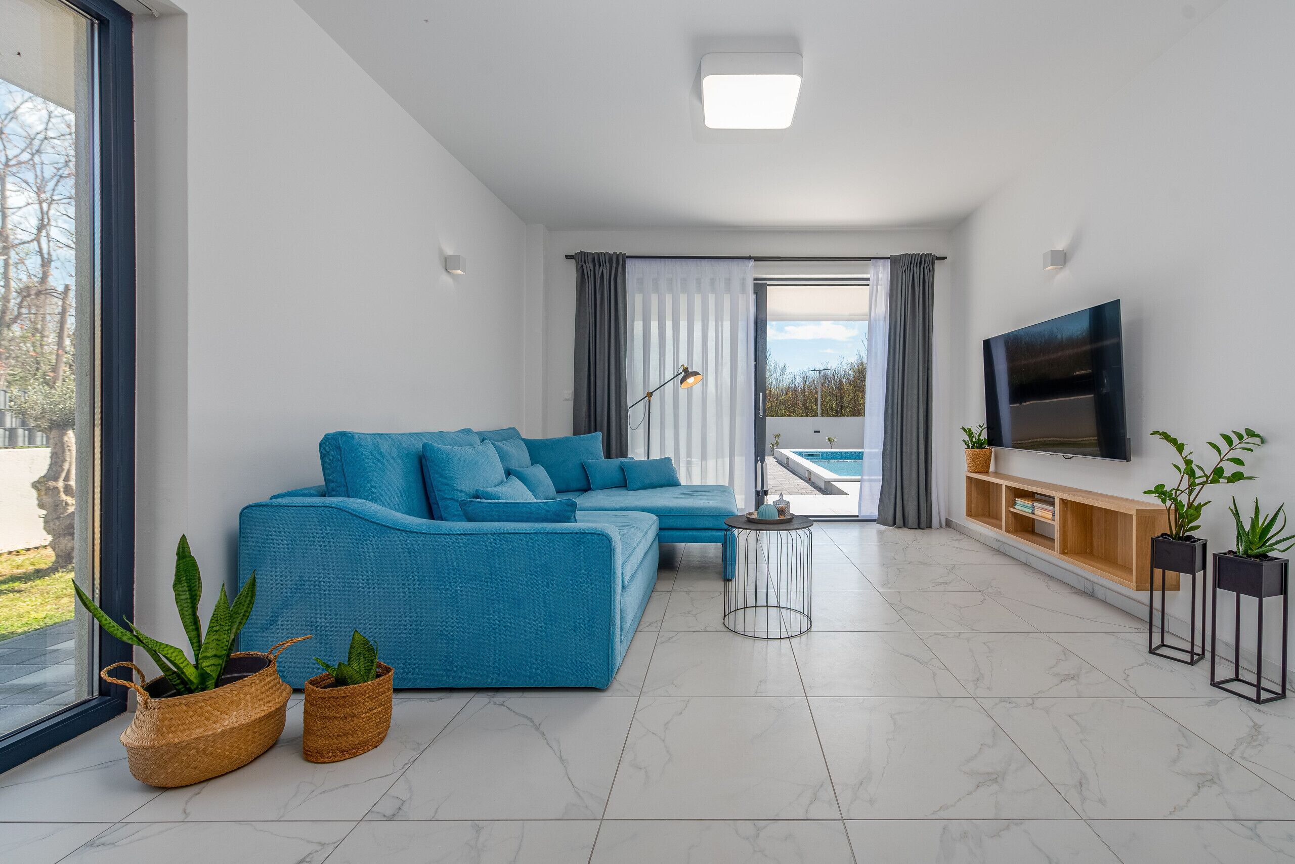 A modern living room with a sectional sofa, a flat-screen TV, and a large window offering a view of the outdoors.