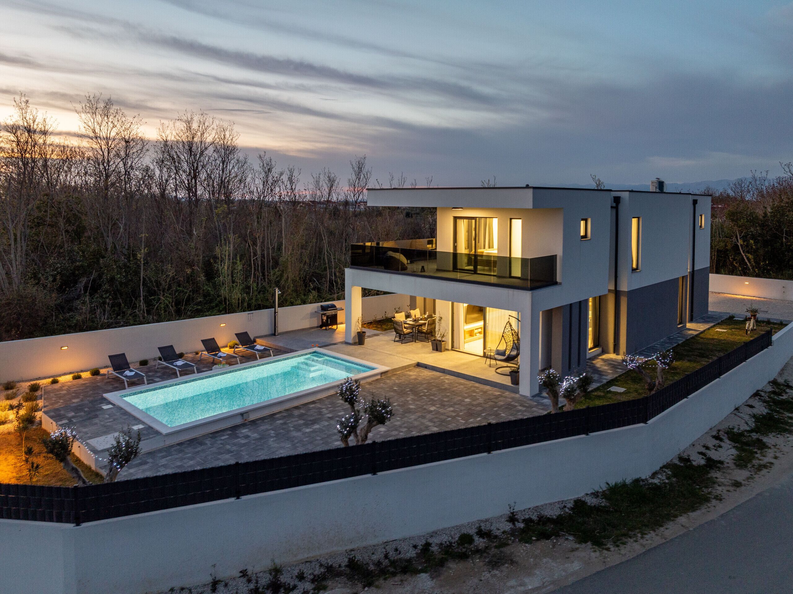 A modern two-story house with a swimming pool, outdoor seating, and a balcony.