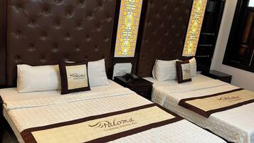 A hotel room with two beds, each with a headboard, white bedding, and a name tag reading "Paloma".