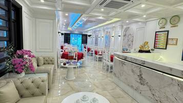 A hotel lobby with a marble reception desk, a seating area with sofas and a round table, and a decorative wall with clocks and framed certificates.