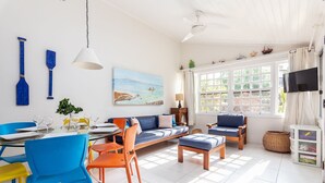 Een lichte woonkamer met een bank, stoelen, een eettafel en een televisie.