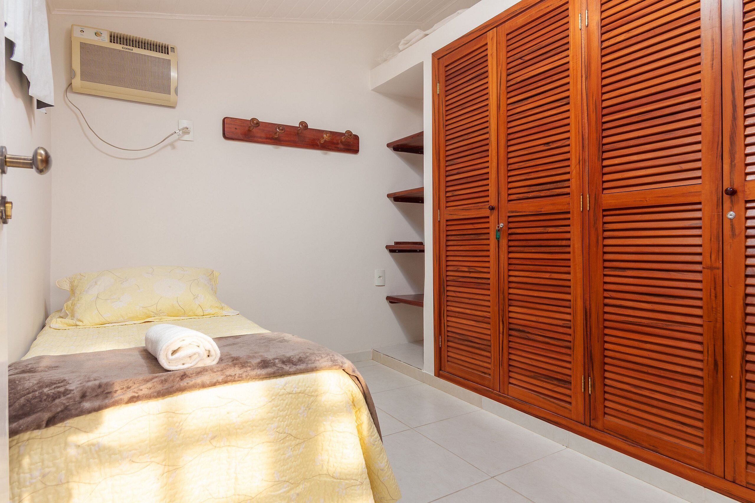 A bedroom with a bed, a wooden wardrobe, a wall-mounted heater, and a towel on the bed.