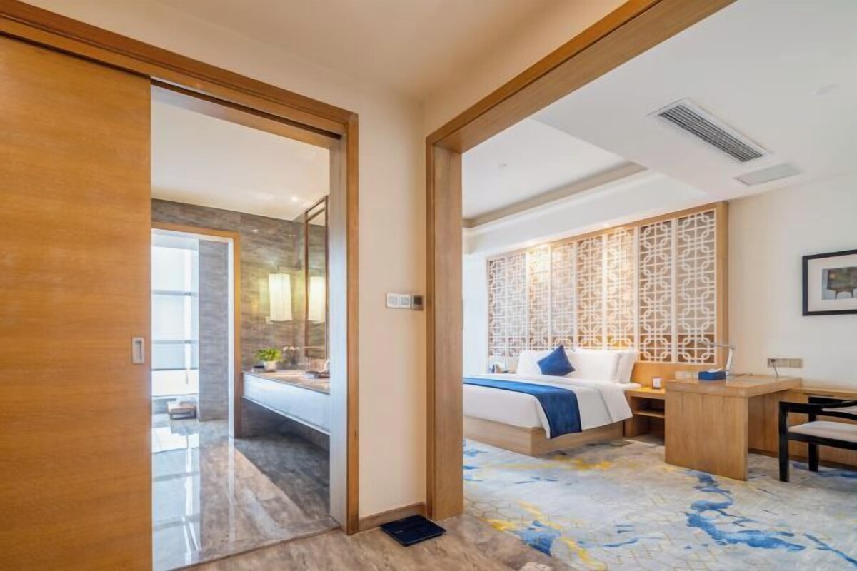 Ein Hotelzimmer mit Holztür, einem Bett mit blau-weißer Bettdecke, einem Schreibtisch und einem dekorativen Raumteiler.