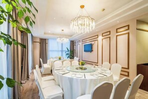 Un salón de conferencias con mesas redondas, sillas blancas y una araña de cristal.