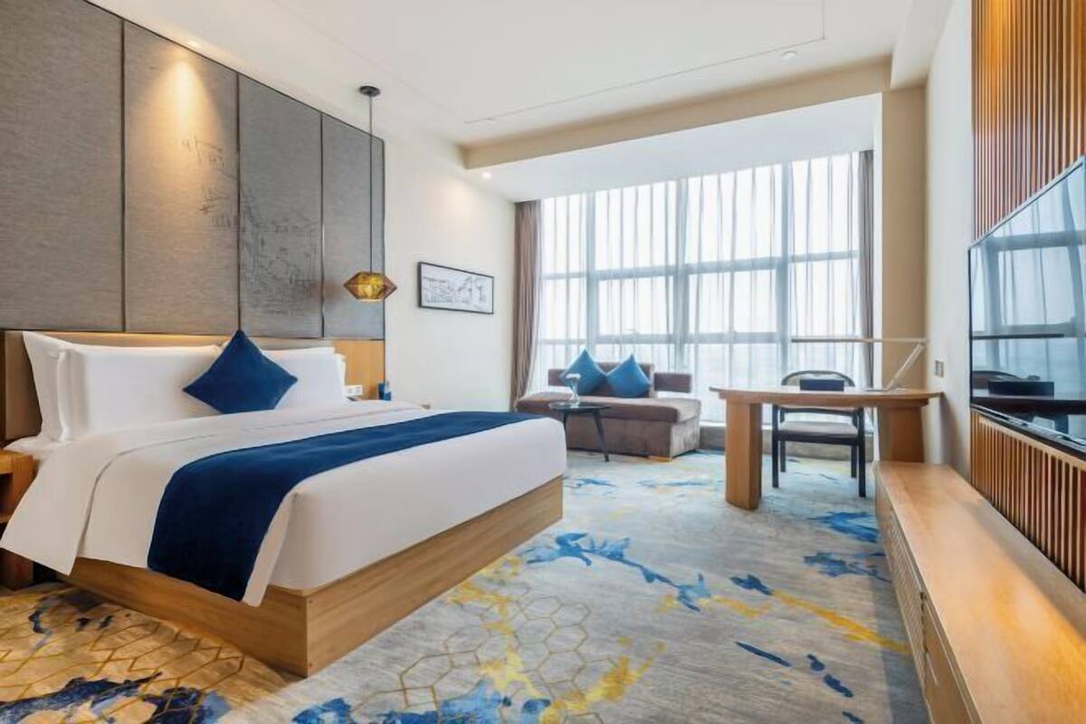 A modern hotel room with a large bed, a sofa, a dining table, and a TV.