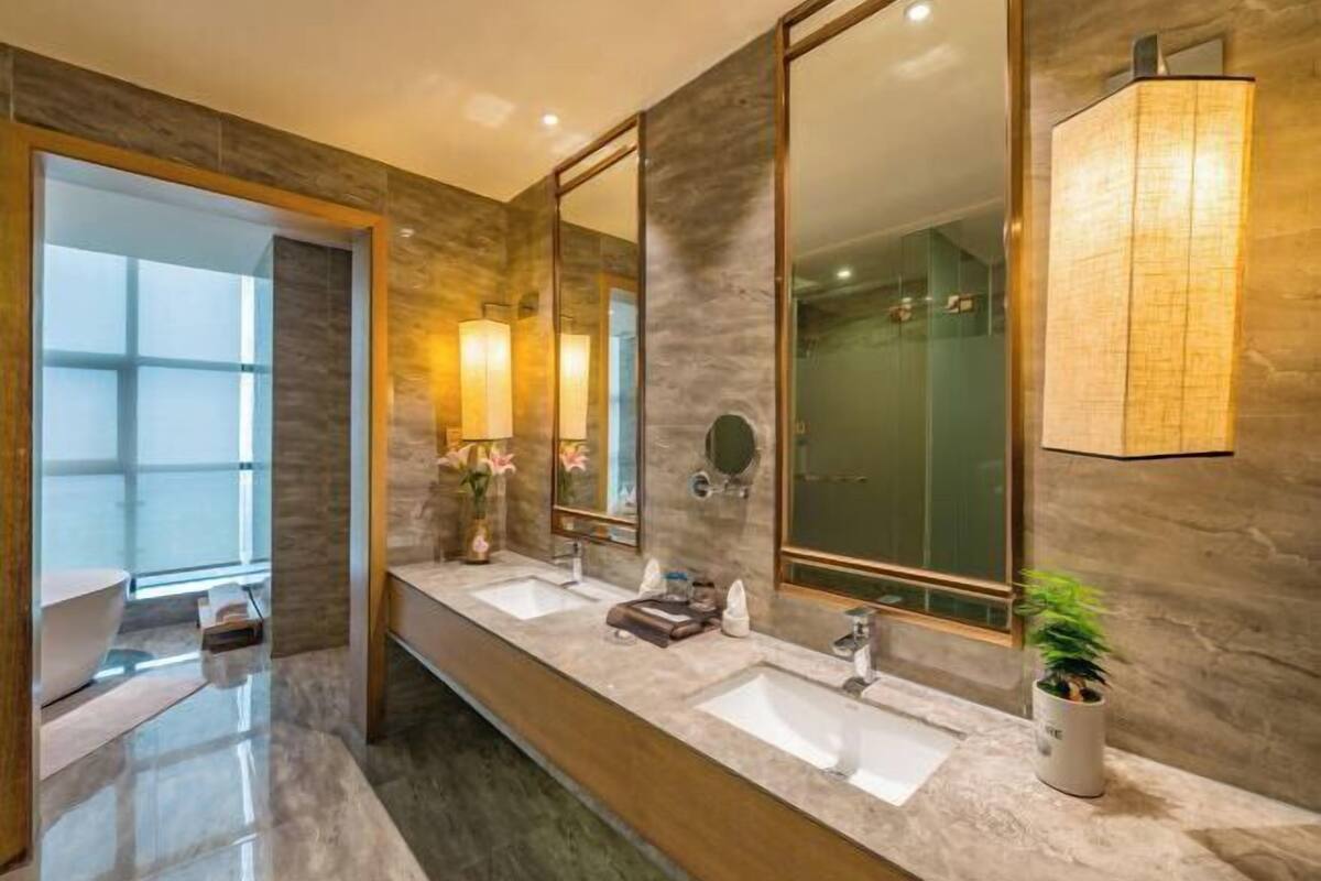 A modern bathroom with two sinks, large mirrors, and a potted plant.