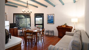 A dining area with a round table, chairs, a chandelier, and a television on a cabinet. - Caletta Nest 38 by Klodge – Pool & tennis (Porto Rotondo)