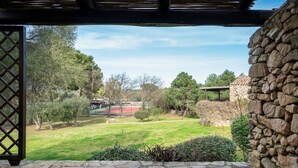 A stone wall and a wooden pergola overlooking a well-maintained garden with a tennis court. - Caletta Nest 38 by Klodge – Pool & tennis (Porto Rotondo)