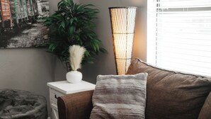 Un canapé marron avec un coussin texturé, une petite table d’appoint blanche ornée d’un vase contenant des plumes d’herbe des pampas, et une grande lampe tressée.