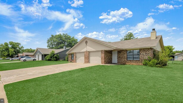 A single-story house with a garage, a brick exterior, and a well-maintained lawn. - Clean, Cozy 2BR, Patio, Near Razorback Stadium (Springdale)