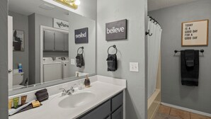 A modern bathroom with a large mirror, vanity, and a shower area. - Clean, Cozy 2BR, Patio, Near Razorback Stadium (Springdale)