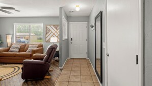 Un salon avec un canapé en cuir marron, un fauteuil marron et un tapis à motifs. On y trouve une porte blanche, un miroir et un interrupteur sur le mur.