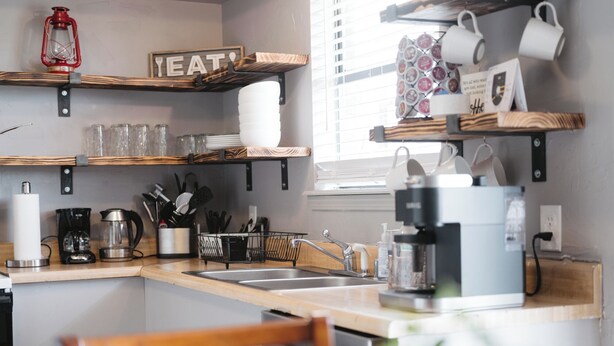 Une cuisine moderne avec des étagères en bois, une machine à café et un coin repas agrémenté d’une chaise en bois.