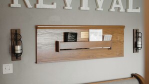 Un mur sur lequel est écrit le mot « RÉVIVAL » en grandes lettres, une étagère en bois avec des livres et une Bible, et deux appliques murales.