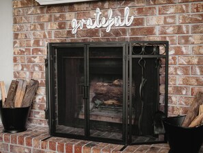 A fireplace with a grate, logs, and a sign that reads "grateful" on a brick wall. - Clean, Cozy 2BR, Patio, Near Razorback Stadium (Springdale)