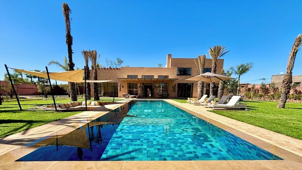 A rectangular swimming pool with a tiled edge, surrounded by a paved deck. There are lounge chairs and umbrellas along the poolside. - Palais Kenza (Marrakech)
