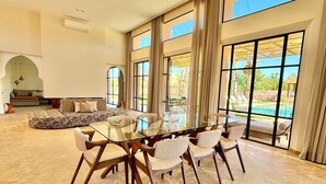 A spacious room with a large glass table surrounded by chairs, a sofa, and a view of a swimming pool. - Palais Kenza (Marrakech)
