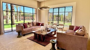 A spacious living room with large windows, a sofa, chairs, and a coffee table. - Palais Kenza (Marrakech)