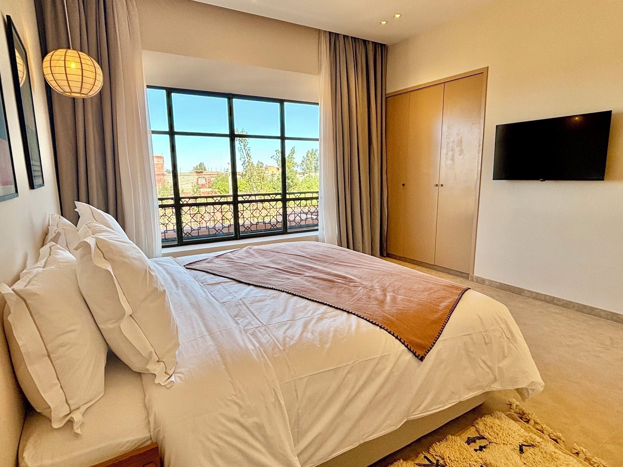 A bedroom with a large bed, a TV, and a window with a view of the outdoors.