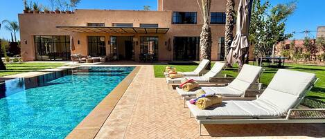 A modern pool area with lounge chairs and a pool, surrounded by a well-maintained lawn and palm trees.