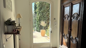 Un pasillo con una puerta blanca que da a un espacio exterior, una planta en maceta, una lámpara y un gran armario de madera.
