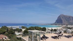 En takterrass med solstolar, ett glastak och utsikt över kusten och ett markant berg.