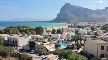 Une ville côtière avec une grande montagne en arrière-plan, une plage et un espace piscine doté de chaises longues.