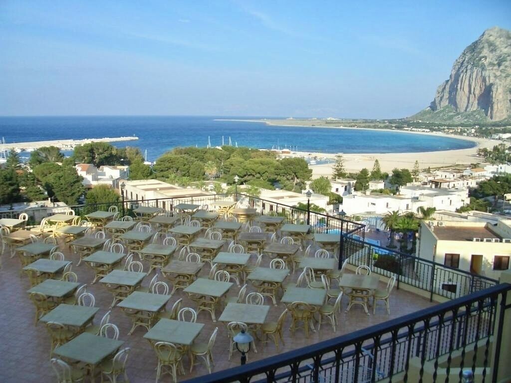 A terrace with outdoor seating overlooking a beach and a mountain.