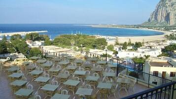 A terrace with outdoor seating overlooking a beach and a mountain.