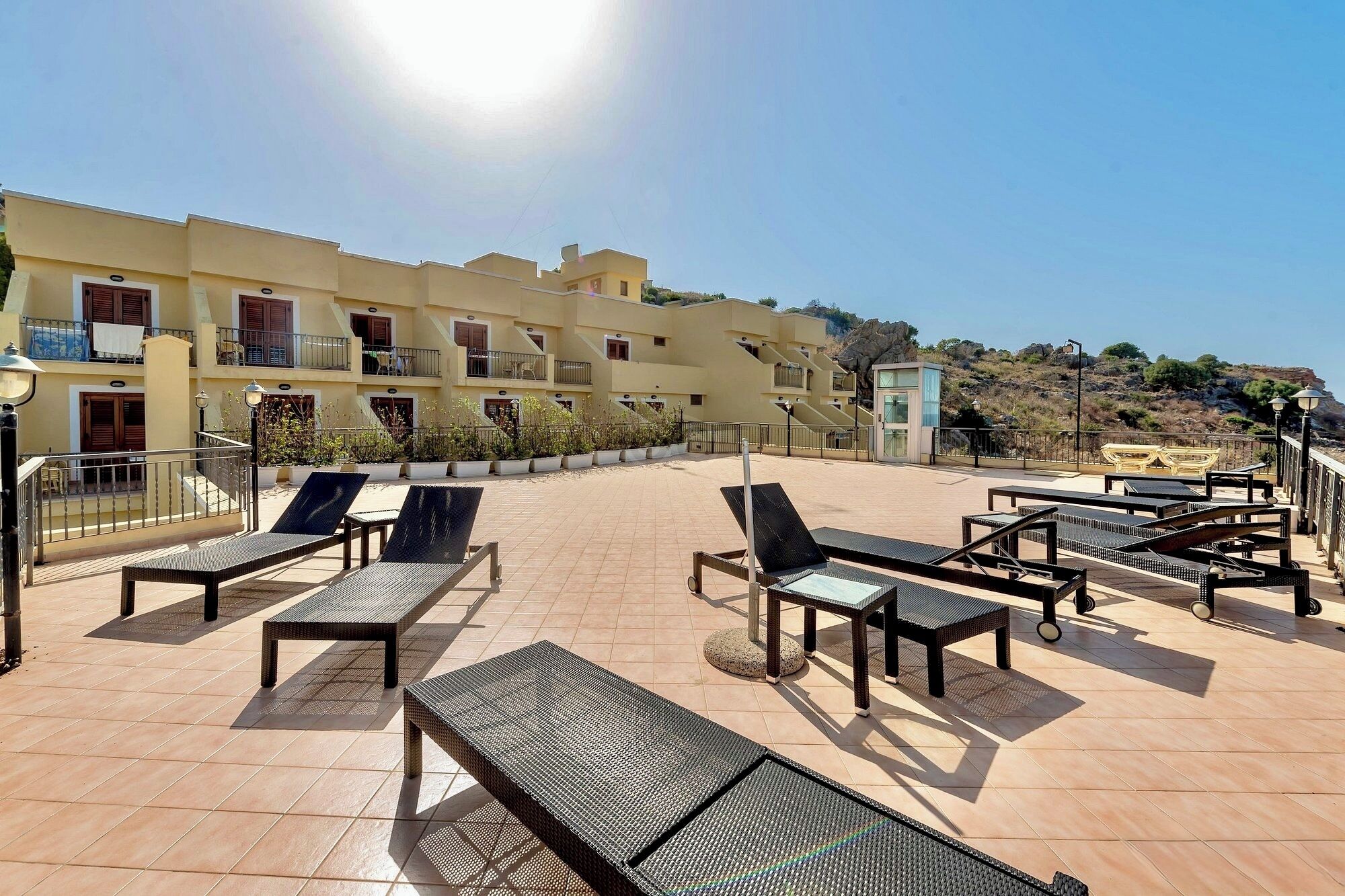 A rooftop terrace with sun loungers and a view of a building with balconies.