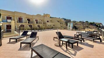 A rooftop terrace with sun loungers and a view of a building with balconies.
