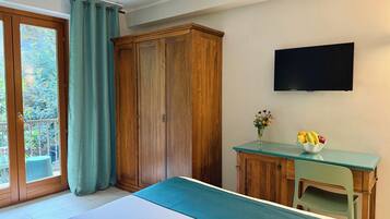 Una camera da letto con un letto, un armadio in legno, una scrivania con un vaso di fiori e una televisione a parete.