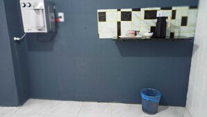 Ein Badezimmer mit blauer Wand, weiß gefliestem Fliesenspiegel, einer Kaffeemaschine und einem blauen Mülleimer.