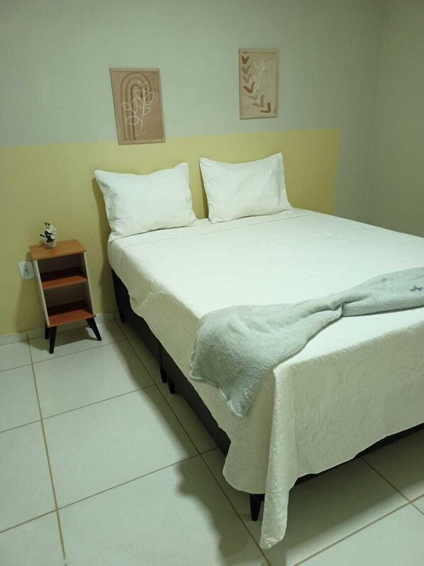 A single-bed room with a white bedspread, a nightstand with a small plant, and two wall-mounted artworks. - NORTE HOTEL GUARACIABA (Guaraciaba do Norte)