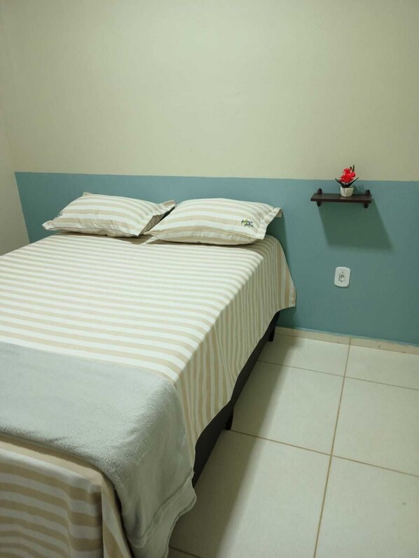 A single bed with striped bedding, a small shelf with a potted plant, and a power outlet on the wall. - NORTE HOTEL GUARACIABA (Guaraciaba do Norte)