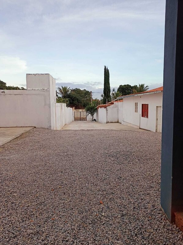 A courtyard with gravel ground, white walls, and a gate leading to a building with a red roof. - NORTE HOTEL GUARACIABA (Guaraciaba do Norte)