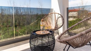 Ein Balkon mit Korbstühlen, einem runden schwarzen Tisch mit einer Flasche und Gläsern sowie Blick ins Grüne.
