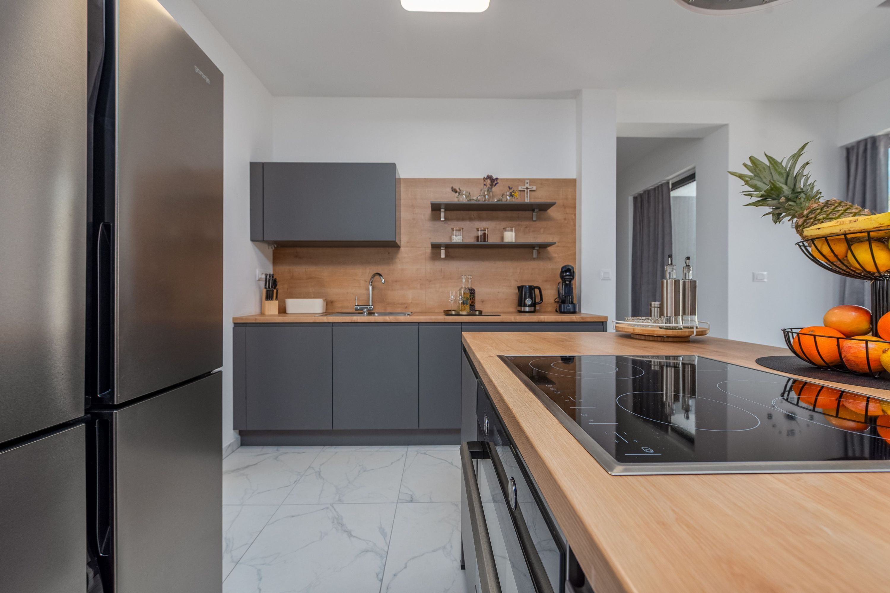 Een moderne keuken met een roestvrijstalen koelkast, grijze kastjes, een houten aanrechtblad en een zwart inductiekookplaat.