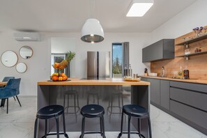 A modern kitchen with a central island, bar stools, and a large window. - Villa Merci Zadarvillas (Privlaka)