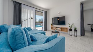 Una sala de estar moderna con un sofá grande, un televisor de pantalla plana y vistas a una piscina.